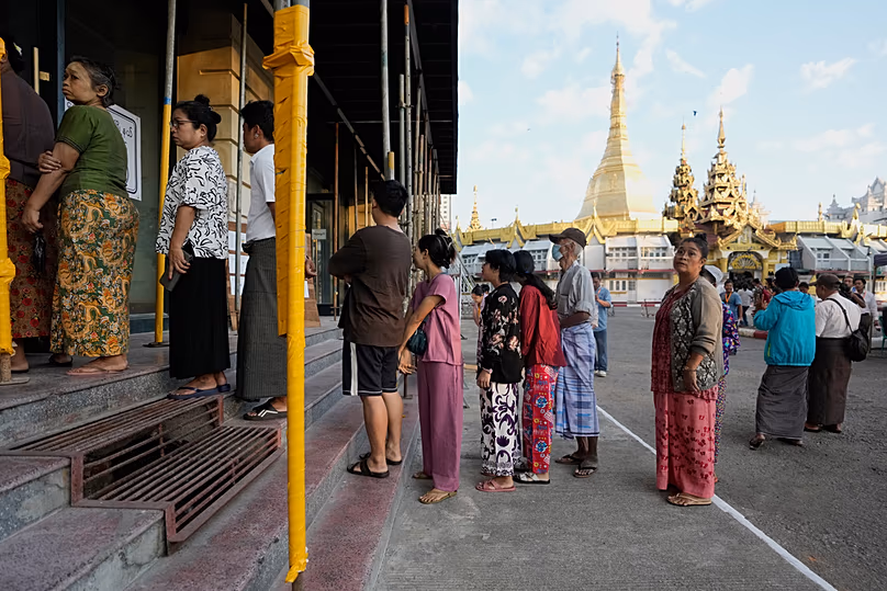 A szavazók 2025. december 28-án, vasárnap Yangonban (Mianmarban) felsorakoznak, hogy leadják voksukat egy szavazóhelyiségben, a háttérben a Sule pagodával. (AP Photo/Thein Zaw)