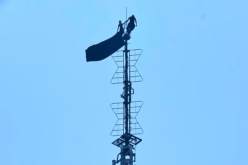 Két ember áll az Empire State Building antennájának csúcsán, miközben transzparenst tartanak a kezükben, 2026. július 1.